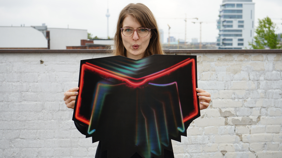 Melanie Gollin hält die Neon Bible. (Foto: Sophie Euler - Arcade Fire Merchandise: V. Kriz)